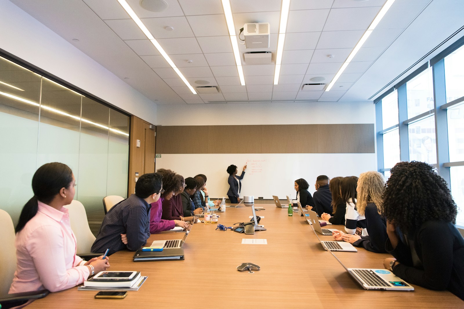 Participants around a conference table listening to a presenter at a whiteboard