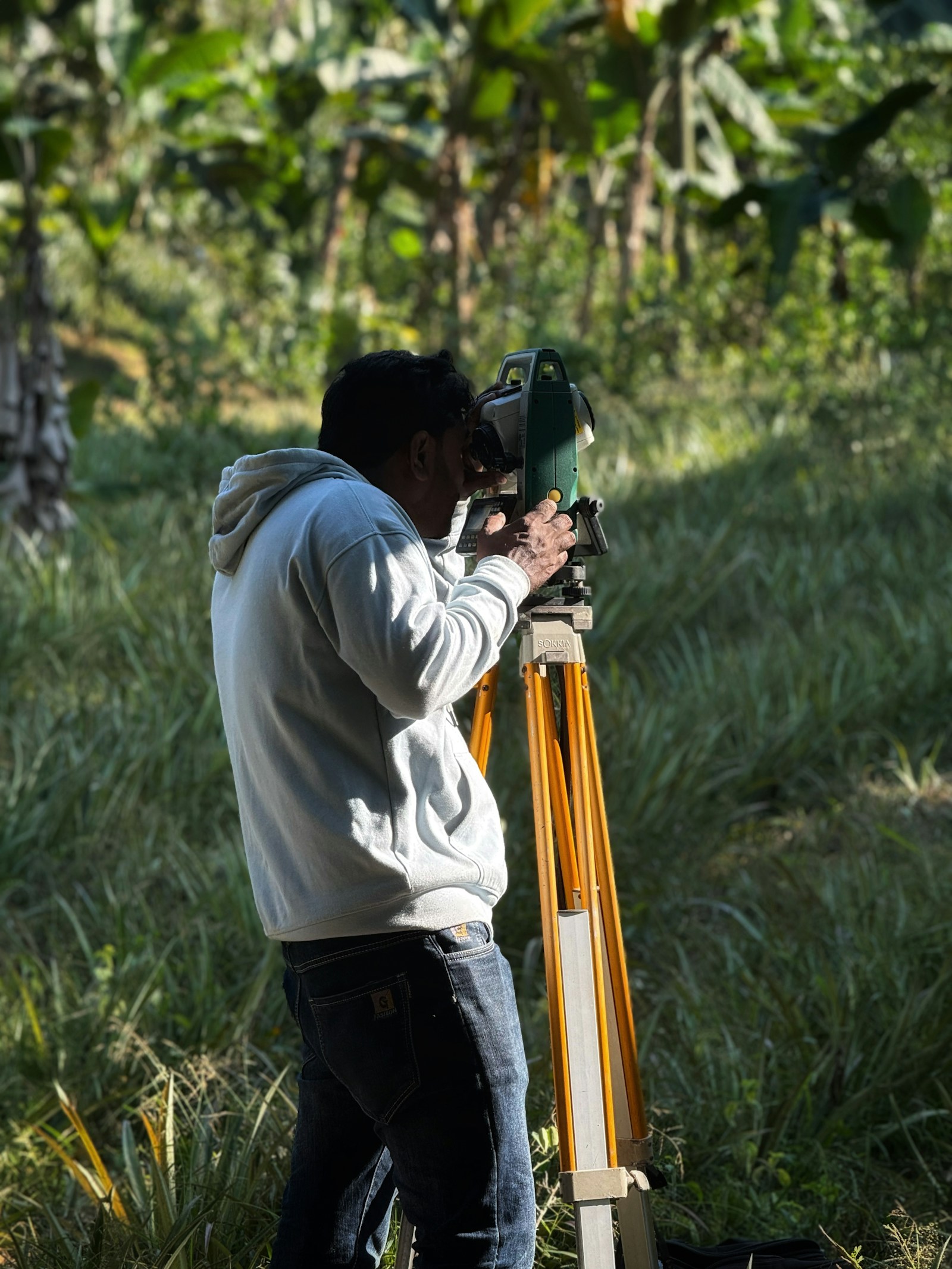 Surveyor using a tripod-mounted instrument in a field