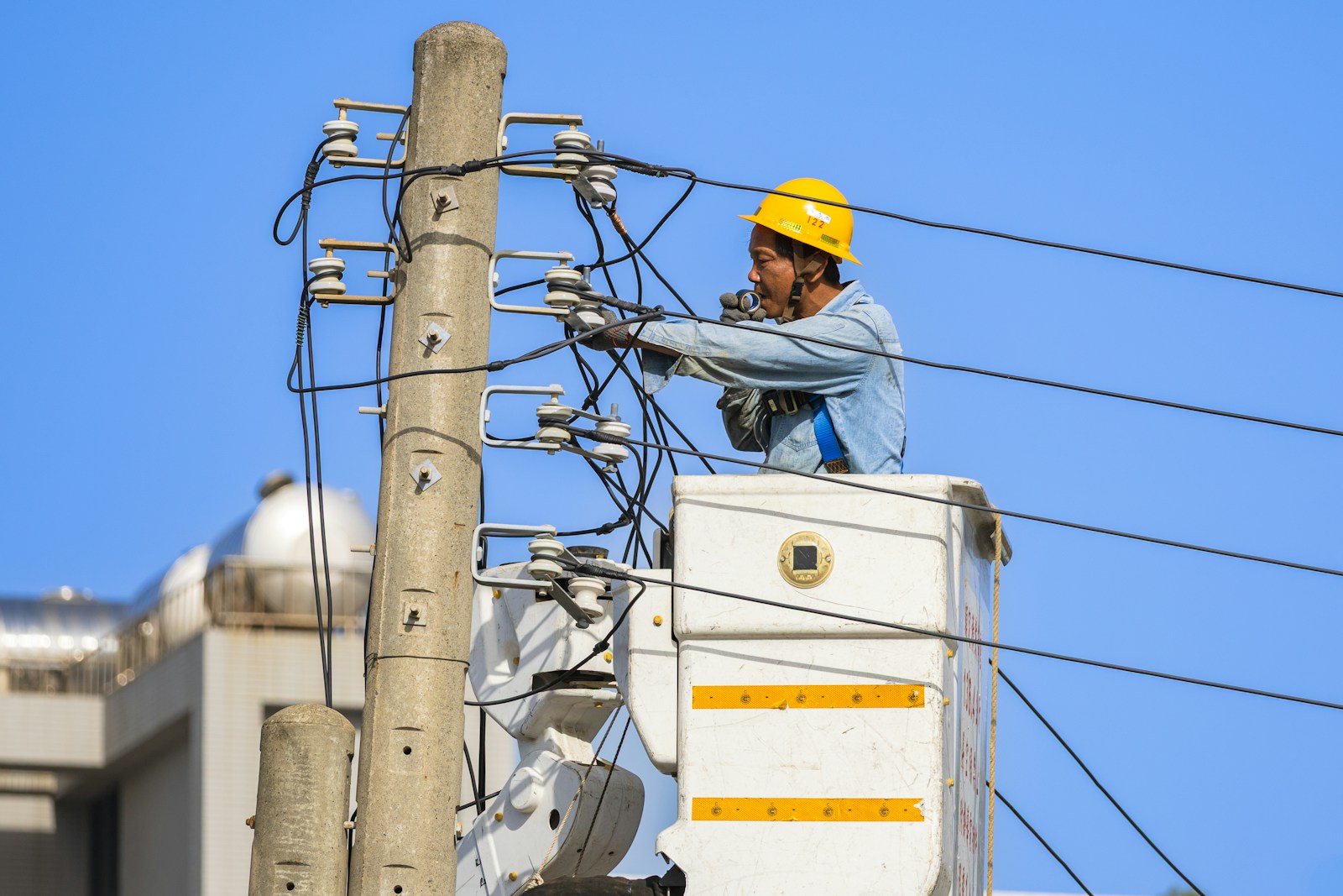 Utility worker maintaining overhead power lines from a lift